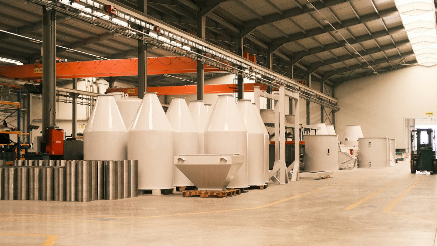 White industrial machinery arranged on a factory floor with an overhead crane.